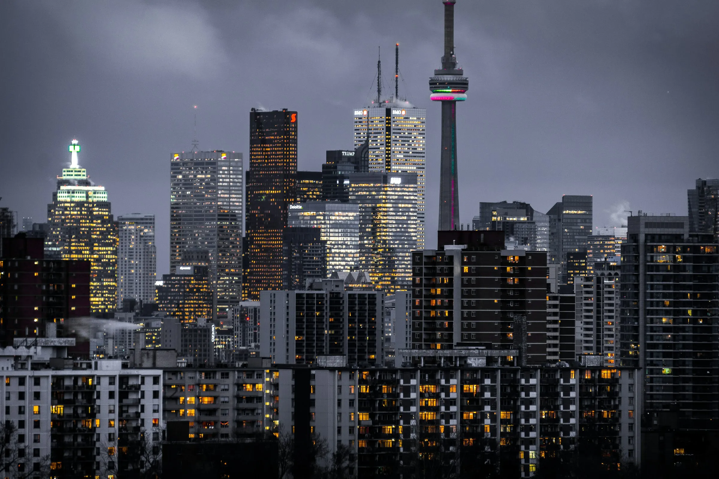 A city skyline at dusk, with lit residential towers in the foreground and office buildings behind.