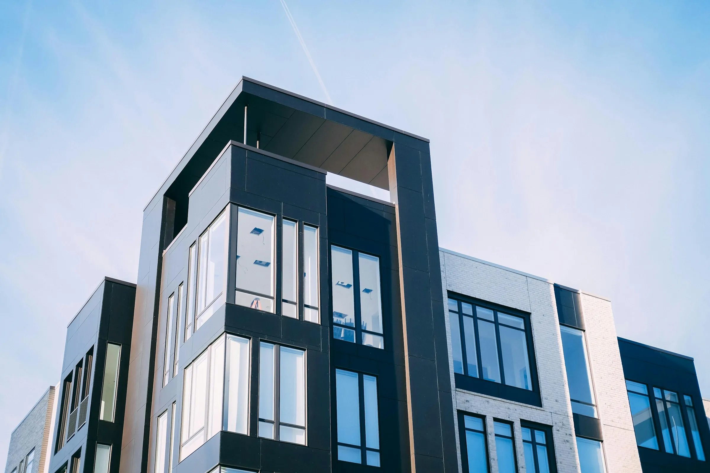 The upper corner of a contemporary low-rise condominium building with dark window frames.
