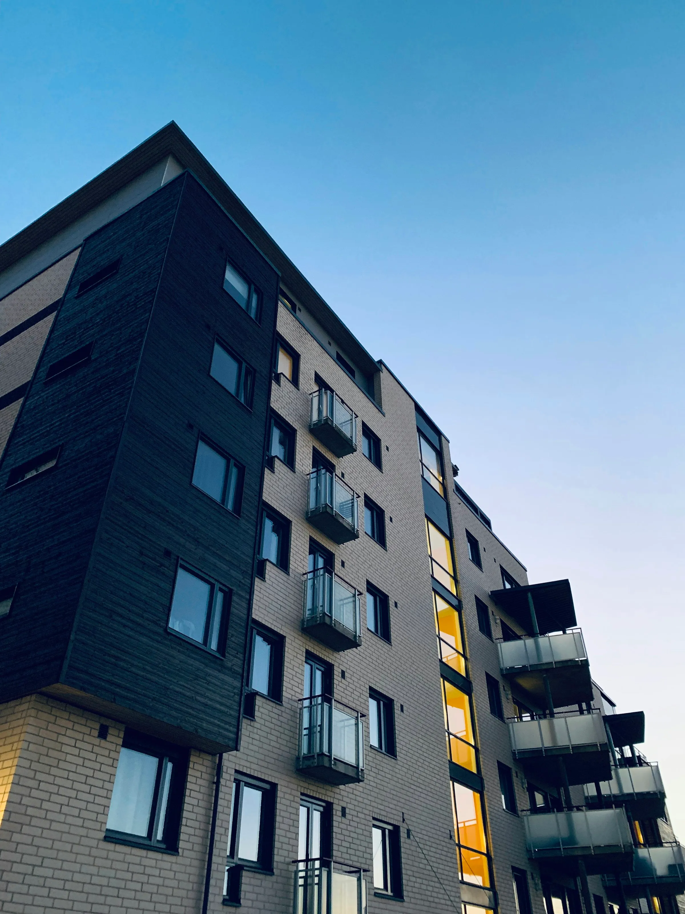 A mid-rise apartment building with tiered balconies, viewed from street level against an evening sky.